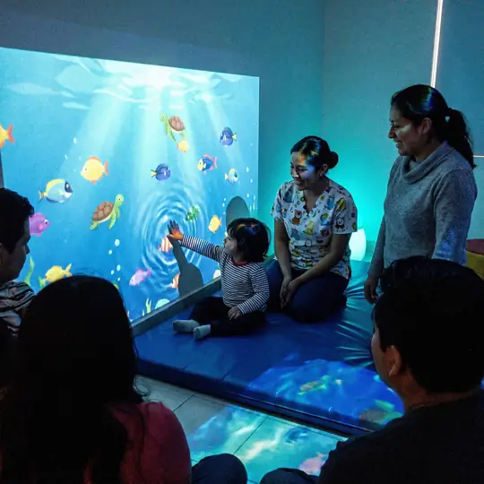 Niña toca una pared con escena submarina interactiva en una sala sensorial pediátrica