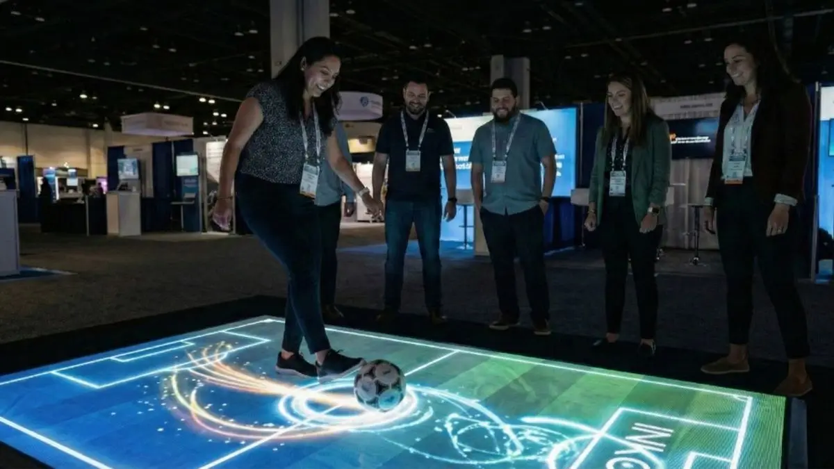 Visitantes juegan con un balón sobre un piso de futbol interactivo en una expo